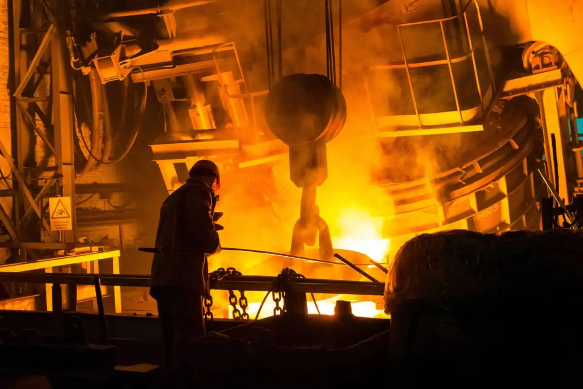 A steelworker stands next to a blast furnace.