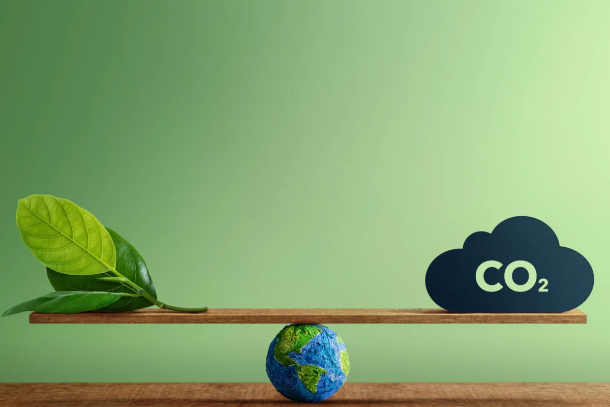 Concept image showing a rocking board balanced on a globe. On the left side of the board is a green leaf. On the right side of the board is a cloud of CO2.